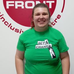 Gracie smiles as she stands in front of wall sticker of the Face Front logo